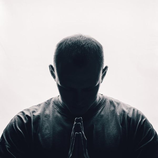 Silhouette of a man in a meditative pose against a bright background.